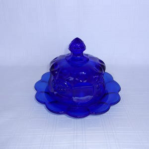 May include: A cobalt blue glass butter dish with a scalloped edge and a domed lid. The dish has a floral design.