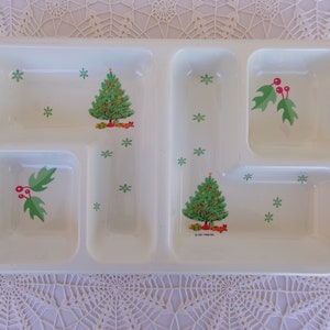 May include: Cream-colored divided serving tray with Christmas-themed illustrations. The tray features a Christmas tree, holly with red berries, and green snowflakes. The tray has five compartments for serving food.