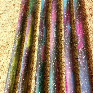 Puede incluir: Seis baquetas de madera pintadas con un dise&ntilde;o de galaxia. Las baquetas est&aacute;n pintadas en tonos de azul, morado y rosa con estrellas blancas. Cada baqueta tiene un nombre escrito en ella: Miley, Cyrus, Spinning, Jenny y otros dos nombres que no son visibles.