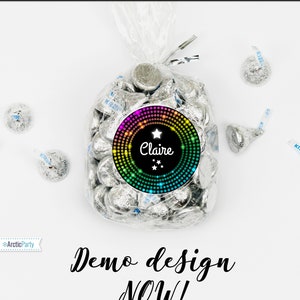 May include: A bag of silver foil-wrapped chocolate kisses with a round sticker on the front. The sticker has a black background with a rainbow circle of dots and a white star. The text "Claire" is written in white cursive font with three white stars below the name.