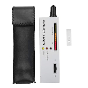 May include: A silver diamond and moissanite tester with a black on/off switch, a red and yellow LED indicator, and a black leather carrying case. The tester has the words "Moissanite/Dia Tester" printed on the side.