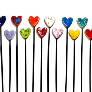 May include: A set of 14 heart-shaped ceramic garden stakes in various colors, including red, blue, green, yellow, and pink. The stakes are attached to black metal rods.