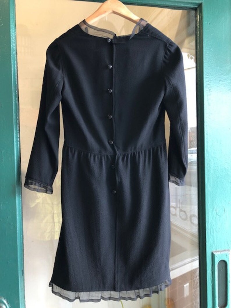 May include: A black dress with long sleeves and a sheer lace trim at the neckline and hem. The dress has a button closure down the back.
