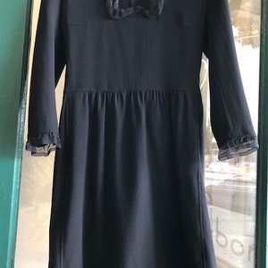 May include: A black dress with a lace trim around the neckline and sleeves. The dress has a fitted bodice and a full skirt.