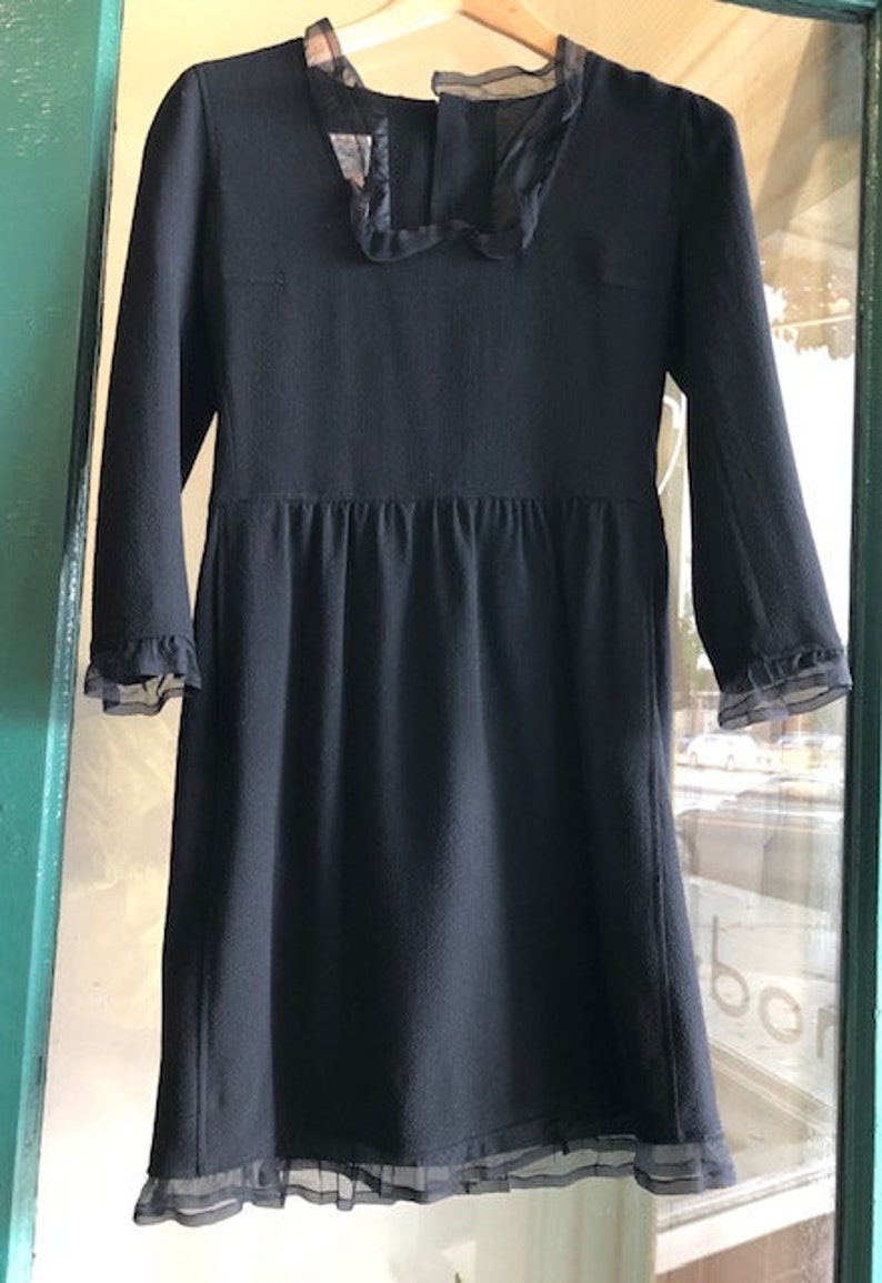 May include: A black dress with a lace trim around the neckline and sleeves. The dress has a fitted bodice and a full skirt.
