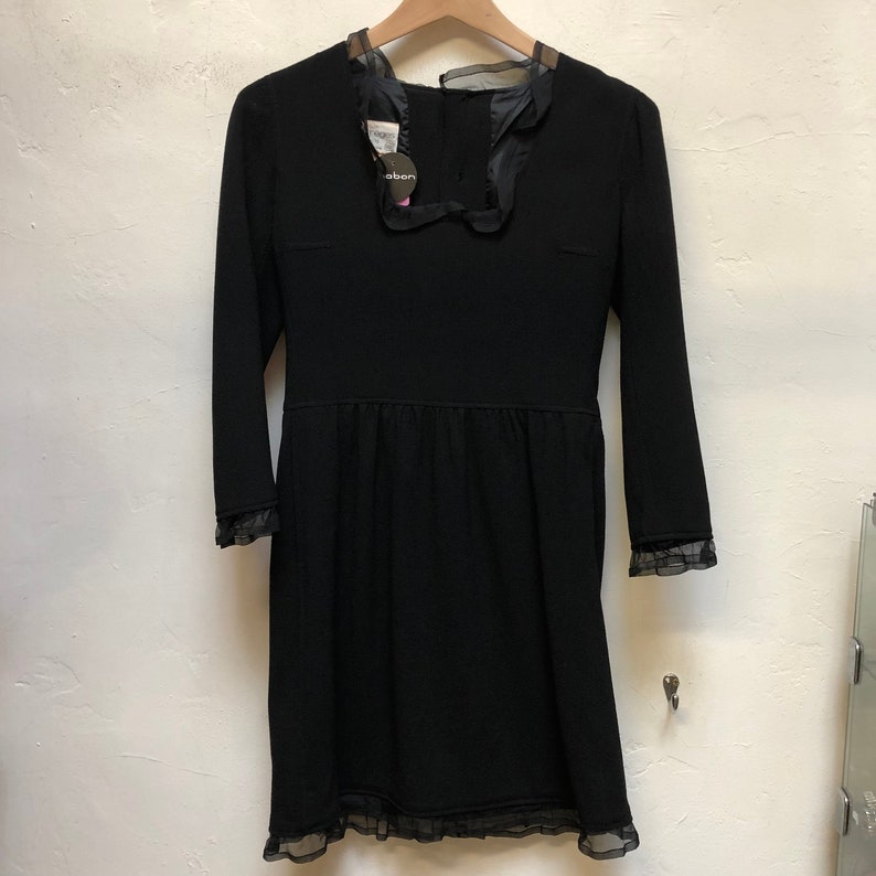 May include: A black dress with long sleeves and a lace trim. The dress has a scoop neckline and a fitted bodice. The dress is hanging on a hanger.