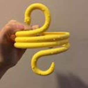 Puede incluir: Percha multi-gancho de plástico amarillo con superficie texturizada. La percha está diseñada para colgar objetos en una pared o puerta.