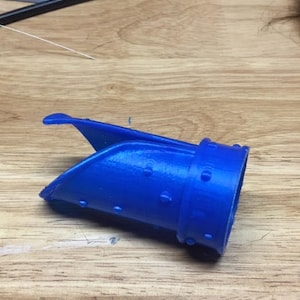 Puede incluir: Un objeto de plástico azul impreso en 3D con un pico curvo y una superficie texturizada. El objeto tiene un agujero en el centro y parece ser una boquilla o un pico.