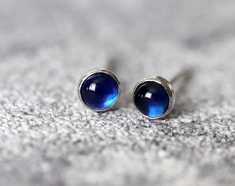 May include: A pair of silver stud earrings with small, round, blue gemstones.