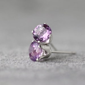 May include: A pair of silver stud earrings with round, faceted amethyst gemstones.