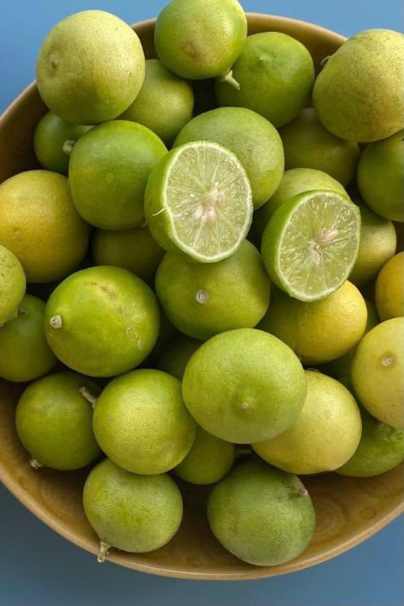 May include: A wooden bowl filled with fresh limes, some whole and some halved. The limes range in color from bright green to yellow-green, with a few showing a yellow hue. The cut limes reveal juicy, pale green flesh.