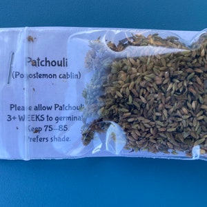May include: A small clear plastic bag containing brown seeds labeled "Patchouli (Pogostemon cablin)". The label also includes instructions for planting the seeds, including a germination time of 3+ weeks and a preferred temperature range of 75-85 degrees Fahrenheit. The label also states that the plant prefers shade.