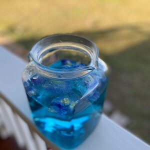 Puede incluir: Una jarra de vidrio transparente llena de t&eacute; azul de flor de guisante mariposa. El t&eacute; es de un color azul vibrante y las flores son visibles en el l&iacute;quido.