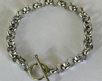May include: A silver-colored chain bracelet with a toggle clasp. The bracelet features a series of interconnected, rounded links. The toggle clasp is a bar that fits through a circular loop to secure the bracelet.