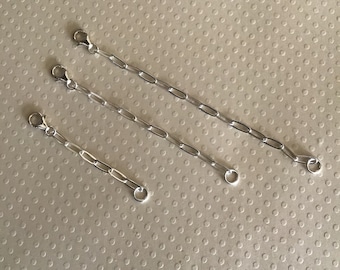May include: Four silver chain extenders of varying lengths, each with a lobster clasp on one end and a jump ring on the other.