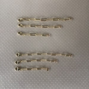 May include: Five gold chain extenders of varying lengths. The extenders are made of a linked chain with a lobster clasp on each end.