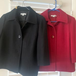 May include: Two short-sleeved jackets, one black and one red, hang on hangers. Both jackets have a classic design with a collar and a single button closure. The jackets appear to be made of a wool blend.
