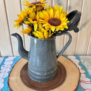 May include: A white ceramic mug with a black handle and the text "But First, Coffee" in a black, handwritten-style font. The mug is on a white surface.