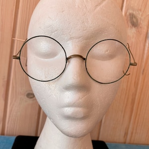 May include: A pair of round, green-framed glasses on a white mannequin head. The glasses have a simple, classic design.