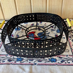 May include: Black metal roasting rack with yellow handles. The rack is designed to fit inside a large oval-shaped baking dish.