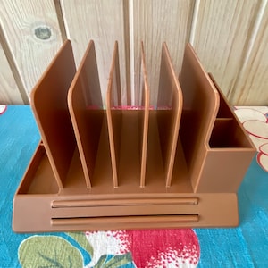 May include: A brown plastic desk organiser with six vertical compartments and a drawer. The organiser has a small compartment on the right side.