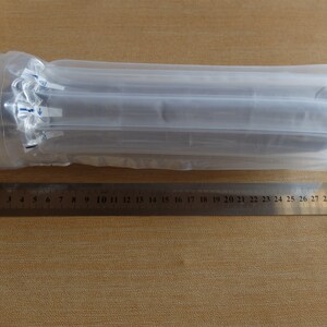 May include: A cylindrical object wrapped in clear plastic packaging, with a ruler alongside. The ruler is marked in centimeters and measures up to 30 cm. The packaging is inflated with air for protection.