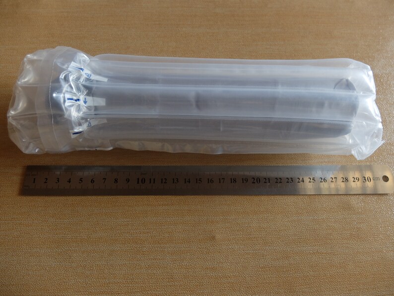 May include: A cylindrical object wrapped in clear plastic packaging, with a ruler alongside. The ruler is marked in centimeters and measures up to 30 cm. The packaging is inflated with air for protection.