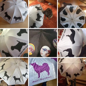 May include: White umbrellas with black dog silhouettes and breed names. One umbrella has a purple dog silhouette with the text "Anana's Norse Goddess". Other umbrellas have different dog breeds. The umbrellas are open.