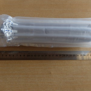 May include: A cylindrical object wrapped in clear plastic packaging. A metal ruler with centimeter markings is placed next to the object. The ruler measures up to 30 cm, or approximately 11.8 inches.