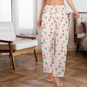 May include: White pajama pants with a colorful paw print pattern. The paw prints are in shades of pink, blue, green, and yellow. The pants have a relaxed fit and a comfortable design.