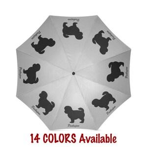 Può includere: Un ombrello grigio con una silhouette bianca di un cane pechinese ripetuta su ogni pannello. Il testo "Pekingese" è scritto su ogni pannello. L'ombrello è aperto e il testo "14 COLORS Available" è scritto sotto l'ombrello.