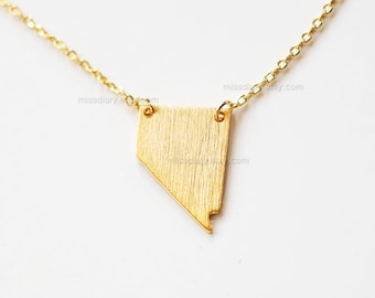 May include: A gold necklace with a brushed gold pendant in the shape of the state of Nevada.
