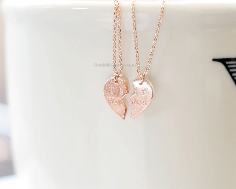 May include: Two rose gold necklaces with heart-shaped pendants that say "Best" and "Friends" on them. The pendants are broken in half, with the two halves fitting together.