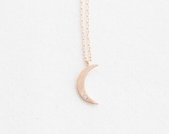 May include: A delicate gold crescent moon necklace with a small clear crystal accent. The necklace features a delicate chain.