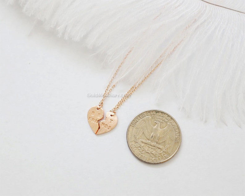 May include: Two gold necklaces with matching heart pendants that say "Best Friends" on them. The necklaces are on a white feather background.