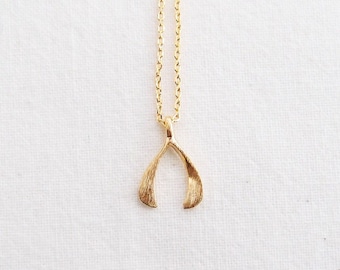 May include: A gold necklace with a wishbone pendant. The pendant is a simple, brushed gold design.