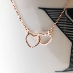 Op de afbeelding: Een delicate ketting van roségoud met twee in elkaar grijpende hart hangers. De harten zijn open en aan de bovenkant met elkaar verbonden.