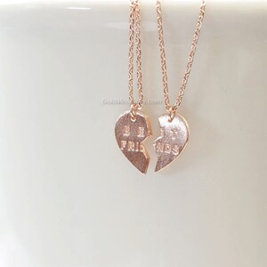 May include: Two gold-toned necklaces with heart-shaped pendants that say "Best Friends" on them. The pendants are broken in half, with one half saying "Best" and the other half saying "Friends".