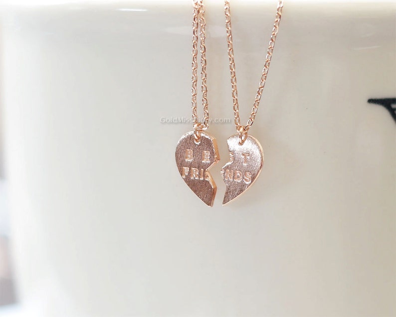 May include: Two gold-toned necklaces with heart-shaped pendants that say "Best Friends" on them. The pendants are broken in half, with one half saying "Best" and the other half saying "Friends".
