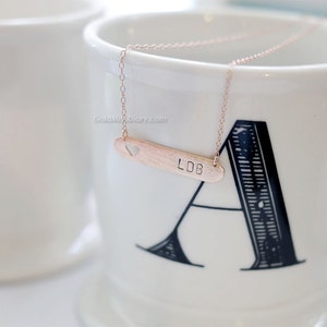 May include: A rose gold necklace with a heart cutout and a bar pendant engraved with the initials "LDB".