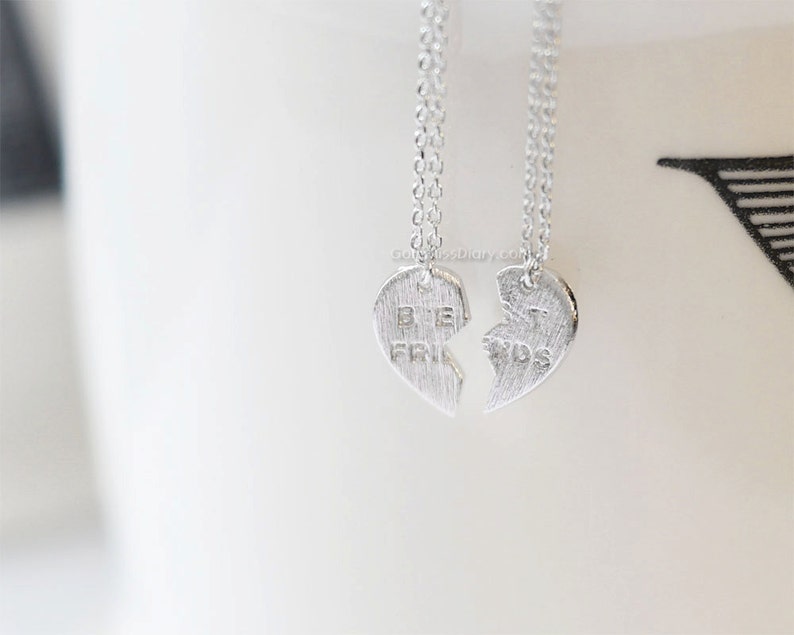 May include: Two silver necklaces with heart-shaped pendants that say "Best Friends" on them. The hearts are broken in half, with one half saying "Best" and the other half saying "Friends".