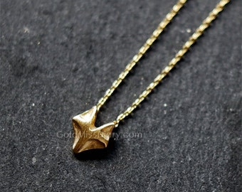 May include: A gold chain necklace with a small, geometric pendant in the shape of a star. The pendant is made of a textured metal and has a slightly rough surface.
