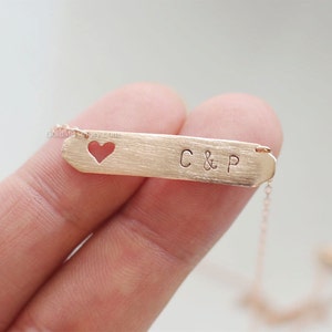 May include: A gold necklace with a heart-shaped cutout and a bar pendant engraved with "C & P".