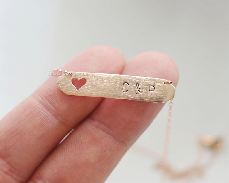 May include: A gold necklace with a heart-shaped cutout and a bar pendant engraved with "C & P".
