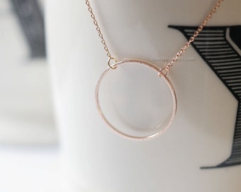 May include: A delicate rose gold necklace with a simple circle pendant. The circle is textured and has a slightly hammered finish.