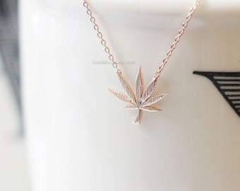 May include: A delicate gold chain necklace with a small, detailed marijuana leaf pendant.