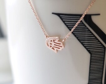 May include: A delicate rose gold necklace with a hamsa hand charm. The hamsa hand is a symbol of protection and good luck.