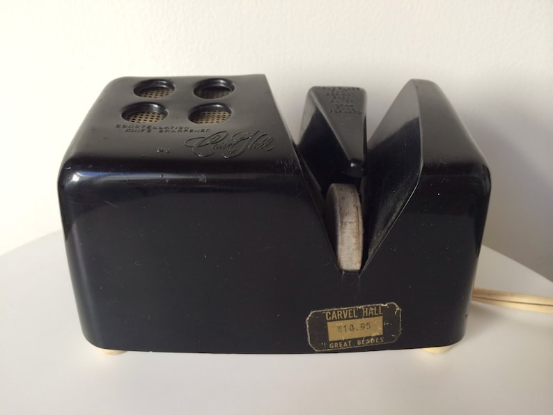 May include: Black electric knife sharpener with a white sharpening stone and a gold label that reads "Carvel Hall $10.95 Great Berries".
