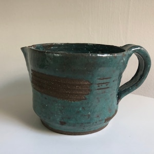 May include: A teal green ceramic pitcher with a brown stripe design. The pitcher has a rounded body and a handle.