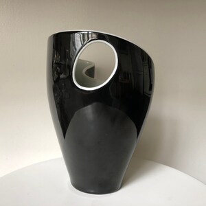May include: A black ceramic vase with a white oval cutout. The vase has a glossy finish and a unique, modern design.